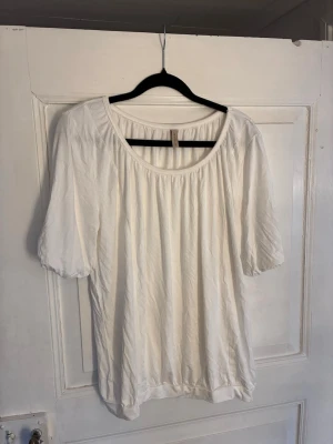 Vit blus från Soyaconcept - Snygg vit blus från Soyaconcept med rund halsringning och lätt puffade korta ärmar. Tillverkad i ett mjukt och tunt tyg som ger en luftig känsla. Perfekt att matcha med jeans eller kjol för en fräsch look.