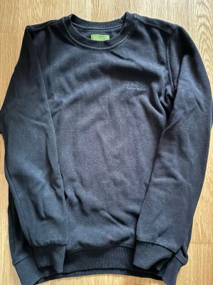 Svart sweatshirt från BOSS - En stilren svart sweatshirt från BOSS med diskret broderad logga på bröstet. Tröjan har rund halsringning, ribbade muddar vid ärmslut och nederkant samt är tillverkad i mjukt bomullsmaterial. Perfekt för en clean och avslappnad look. Pris går att diskutera 