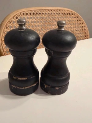 Svarta peppar- och saltkvarnar - Säljer ett set med två klassiska kvarnar i svart trä med silverfärgade metalltoppar. De har en rundad form och är perfekta för att mala peppar och salt. Passar snyggt på matbordet och ger en stilren känsla till köket. Ca 11.5cm