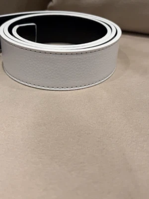 Snyggt Vitt skärp. - Stilrent vitt skärp i skinn med slät yta och diskreta sömmar längs kanterna. Perfekt för att lyfta vilken outfit som helst med en clean och modern look. Bältet är brett.