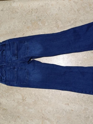 Mörkblå bootcut jeans - Säljer ett par mörkblå bootcut jeans med klassisk femficksdesign och knappgylf. Jeansen har en lätt utsvängd passform nedtill och är tillverkade i mjukt denimtyg. Perfekta för en avslappnad och trendig look. Har knappt använts för jag tycker inte om hur de ser ut.