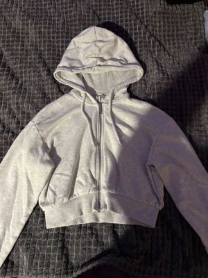 Ljusgrå croppad hoodie med dragkedja - Snygg ljusgrå hoodie i croppad modell med dragkedja framtill och huva. Perfekt för en avslappnad och trendig look. Tillverkad i mjukt sweatshirtmaterial som är skönt mot huden.