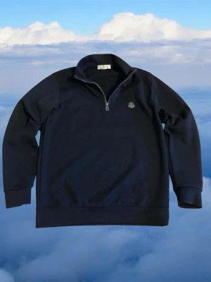 Svart halfzip hoodie från Moncler - Svart hoodie från Moncler med halv dragkedja och diskret logga på bröstet. Klassisk och stilren design med ribbade muddar och hög krage. Perfekt för dig som gillar exklusiva streetwear-plagg.