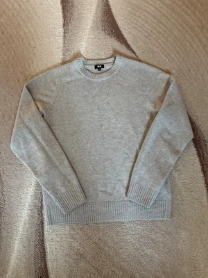 Ljusgrå stickad tröja från Uniqlo - En stilren ljusgrå stickad tröja från Uniqlo med rund halsringning och ribbade muddar vid ärmslut och nederkant. Perfekt för lager-på-lager och enkel att matcha med olika outfits. Materialet känns mjukt och bekvämt.