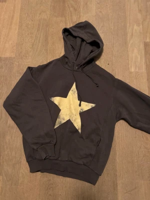Grå bershka hoodie med stjärna - Säljer en grå hoodie med stor vit stjärna på framsidan och texten 'Los Angeles 1998' i vitt på ryggen. Hoodien har huva med dragsko och ribbade muddar vid ärmar och nederkant. Perfekt för dig som gillar streetwear och coola tryck.