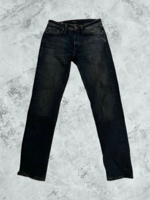Mörkblå jeans från Jack & Jones - Snygga mörkblå jeans från Jack & Jones med klassisk femficksdesign och raka ben. Jeansen har diskreta slitningar och en svart patch med logga bak i midjan. Perfekta för en stilren och avslappnad look. Aldrig använt. 