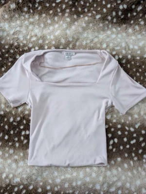 Ljusrosa ribbad topp från new yorker - Supersöt ljusrosa topp från new yorker med ribbad struktur och fyrkantig urringning. Kortärmad och croppad modell som passar perfekt till jeans eller kjol. Enkel och stilren design som är lätt att matcha.