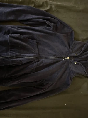 Svart hoodie med dragkedja - Mysig svart hoodie i mjukt tyg med dragkedja framtill och stor huva. Har två stora fickor på magen och metallringar vid snörningen. Perfekt för en chill och avslappnad stil.