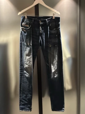 Mörkblå slitna jeans från Diesel - PRISET KAN DISKUTERAS!!!     Säljer ett par mörkblå jeans från Diesel med snygga slitningar och detaljerade rivna partier. Klassisk femficksmodell med logotyp på myntfickan. Jeansen har smal passform och är tillverkade i denim. Hör av er vid frågor eller prisförslag! 🤝