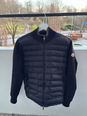 Svart pufferjacka från Moncler - Snygg svart pufferjacka från Moncler med quiltad front och stickade ärmar. Jackan har hög krage, två dragkedjeförsedda fickor och Moncler-logga på ärmen. Perfekt för kalla dagar och ger en clean streetwear-look. Säljer då ja inte använder den. Skriv vid funderingar eller frågor!