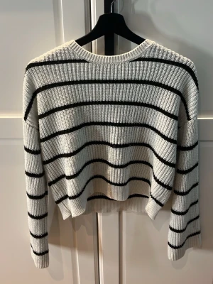 Vit stickad tröja med svarta ränder - Säljer en vit stickad tröja från Kappahl med svarta horisontella ränder. Tröjan har rund halsringning och en avslappnad passform. Perfekt för dig som gillar klassiska ränder och mjuka material.