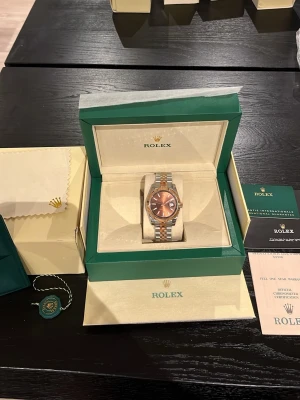  Datejust brun/silver/guld - Säljer en exklusiv Datejust med brun urtavla och datumvisning. Klockan har en tvåfärgad länk i silver och guld, samt en räfflad bezel i guld. Levereras i originalbox med certifikat och tillbehör. Perfekt för dig som vill ha en lyxig accessoar.