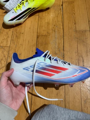 Adidas F50 fotbollsskor vit/blå/röd - Säljer ett par Adidas  F50 PRO MG fotbollsskor. Storlek 44. Nytt skick oanvända. Nypris 1649kr.