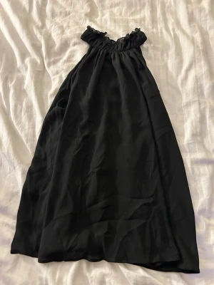 Svart axelbandslös tubtopp från H&M - Svart axelbandslös tubtopp från H&M med volangdetalj upptill. Toppens material är lätt och faller snyggt, perfekt för dig som gillar en enkel och stilren look.