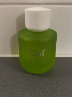 Pistachio Butter parfymflaska - En snygg parfymflaska i frostat grönt glas med vit kork från Weekend Collection. Flaskan har texten 'Pistachio Butter' på framsidan och en rund, modern form som känns både trendig och unik. Perfekt för dig som gillar coola och färgglada detaljer på sminkbordet.