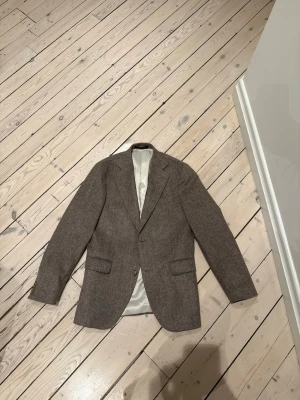 Beige Oscar Jacobson ullkavaj med klassisk passform som aldrig har använts - Snygg beige Oscar Jacobson kavaj i ull med två knappar framtill och två fickor med lock. Kavajen har aldrig använts. Klassisk passform och helfodrad insida i ljus färg. Perfekt för en stilren och tidlös look. Passar till både skjorta och t-shirt.