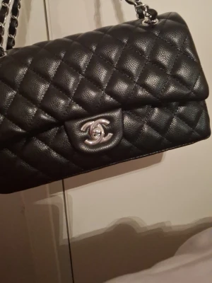 svart andväska - Säljer en ikonisk svart quiltad handväska . Väskan är tillverkad med klassiskt rutmönster och har en tidlös, elegant design som passar perfekt till alla outfits.