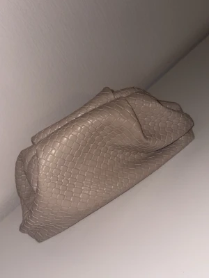 Beige pouch - Stilren beige kuvertväska med ormmönstrad struktur. Väskan har en mjuk, puffig form . Perfekt för att lyfta outfits , väskan är i fint skick och säljs för 230 kr