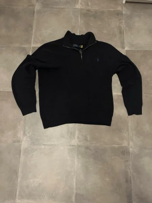 Marinblå  halvzip tröja från Polo Ralph Lauren - Säljer en marinblå tröja med halv dragkedja från Polo Ralph Lauren. Tröjan har lång ärm och den klassiska broderade loggan på bröstet. Perfekt för dig som gillar stilrena och tidlösa plagg. Materialet känns mjukt och bekvämt.