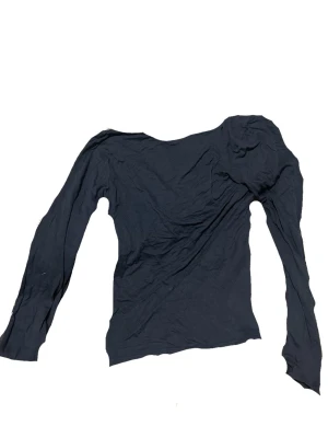 Svart långärmad topp med öppen rygg - En svart långärmad topp med öppen rygg, med figurnära passform. Perfekt att styla med jeans eller kjol för en enkel och clean look. Tillverkad i mjukt material som känns skönt mot huden.