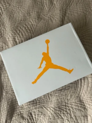Air Jordan 3 Retro Vit/Orange - Säljer ett par Air Jordan 3 Retro sneakers i vitt läder med orange och svarta detaljer samt klassiskt elephant print vid tå och häl. Skorna har en chunky sula och ikonisk Jumpman-logga. Perfekta för dig som vill sticka ut med stilrena och sportiga sneakers.