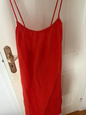 Sommarklänning - Säljer en enkel och snygg orange/korall klänning med tunna axelband och rak passform. Klänningen är kort och har en luftig känsla, perfekt för varma dagar. Materialet känns lätt och passar bra till sommaren.