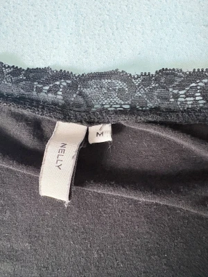 Svart topp med spets från Nelly - Snygg svart från Nelly med långa ärmar och v-ringad halsringning dekorerad med spetsdetaljer