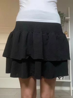 Svart volangkjol - Säljer en svart kort volang kjol med resår i midjan. Kjolen har en luftig och lätt struktur som ger en cool och avslappnad look. Säljer den då den inte kommit så mycket till användning,kontakta mig om ni vill ha fler bilder eller undrar över något💕