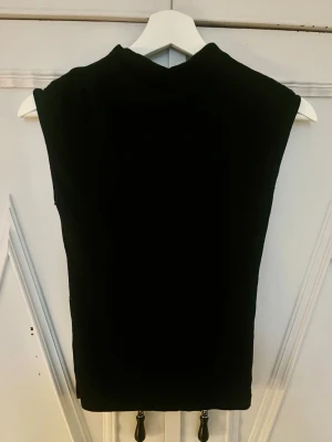 Svart ärmlös croppad topp - Snygg svart croppad topp med hög hals och ärmlös design. Perfekt att matcha med höga jeans eller kjol för en trendig look. Enkel och stilren modell utan synliga detaljer eller mönster.