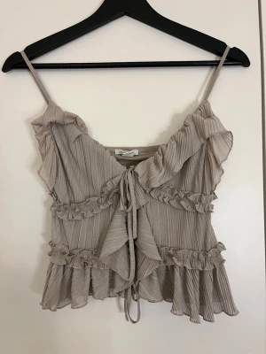 Beige volang topp med knyt - Supersöt beige linnetopp med tunna axelband, volangdetaljer och knyt framtill. 
