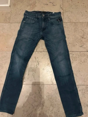 Blå slim fit jeans från replay! - Snygga blå slim fit jeans från replay med klassisk femficksmodell. Jeansen har raka ben och kontrastsömmar samt replay broderingen på bakfickorna. Skicket ör mycket bra. Waist 29. Passar dig som är 170-175. Modellen är anbass