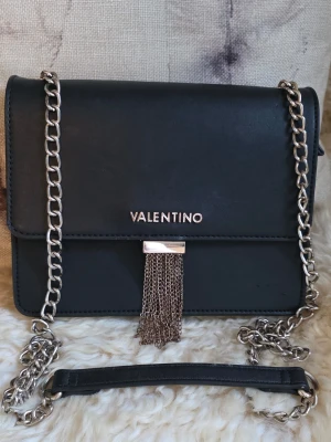 Valentino - Snygg svart axelväska från Valentino i fint skick. Väskan har en stilren, fyrkantig form och är gjord i ett slätt konstläder. Perfekt accessoar för att lyfta din outfit.