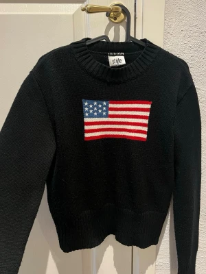 Style svart tröja - Svart tröja med rund halsringning och långa ärmar. Tröjan har en stickad amerikansk flagga framtill som motiv. Storlek M/L men skulle säga att den mer är storlek S!  Mycket gott skick.