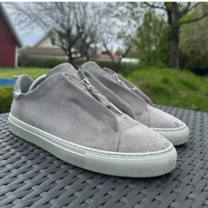 Grå sneakers med dragkedja - Säljer ett par stilrena grå sneakers i mocka med dragkedja framtill. Skorna är från Axel arigato nypris 2600. Bra skick förutom fläcken på bilden (dock inget man tänker på). Pris kan förhandlas