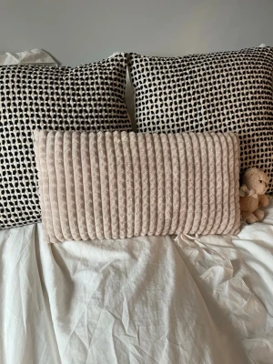 Beige rektangulär prydnadskudde - Mysig beige prydnadskudde i rektangulär form med ribbad, mjuk sammetstextur. Kudden har en stilren och modern look som passar perfekt i soffan eller sängen för extra komfort och dekoration.