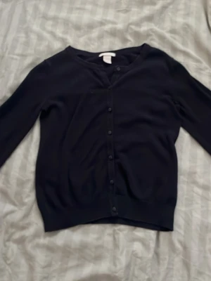 Svart basic kofta med knappar - En stilren svart kofta med rund halsringning och knäppning framtill. Koftan har långa ärmar och ribbade muddar vid ärmslut och nederkant. Perfekt att slänga över en t-shirt eller klänning för en enkel och clean look.