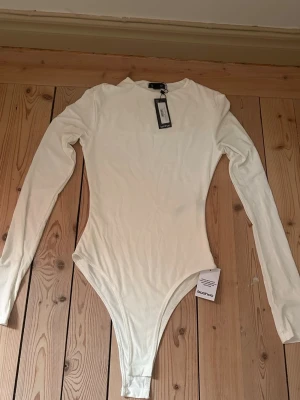 Vit långärmad body från Boohoo - Snygg vit body från Boohoo som tyvärr aldrig kommit till användning. Köpt förra sommaren. Den är i ett  mjukt och stretchigt material som sitter tajt mot kroppen. Perfekt att styla med jeans eller kjol för en clean look. 💕
