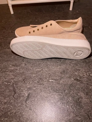 Beige/rosa sneakers - Stilrena beige sneakers från H&M med lågt skaft och vita sulor. Skorna har guldfärgade öljetter och är tillverkade i ett mjukt tygmaterial. Perfekta för en clean och enkel look. Saknar snören!!!