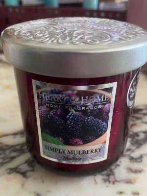 Heart & Home doftljus mullbär - Säljer ett doftljus från Heart & Home i doften Simply Mulberry. Ljuset kommer i en mörklila glasburk med dekorativt silverlock och etikett med mullbärsmotiv. Perfekt för att skapa mysig stämning hemma.