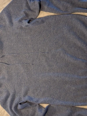 Blå hoodie från Soft Goat - Mysig blå hoodie från Soft Goat i mjukt material, troligen kashmirblandning. Klassisk modell med huva och dragsko, perfekt för chill dagar. Enkel och stilren design utan tryck eller detaljer, passar till det mesta.