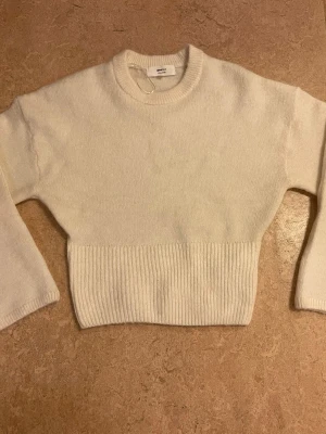 Vit stickad tröja från Gina Tricot - Mysig vit stickad tröja från Gina Tricot med rund halsringning och bred ribbad kant nedtill. Tröjan har lång ärm och är tillverkad i en mjuk ullblandning. Enkel och stilren design som passar till det mesta.