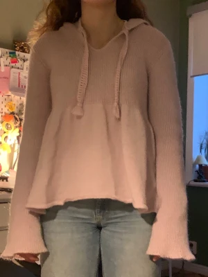 Ljuslila stickad hoodie - Mysig ljuslila stickad hoodie med långa ärmar och dragsko i huvan. Tröjan har en avslappnad passform och lätt utsvängda ärmslut. Perfekt för dig som gillar en chill och trendig stil.