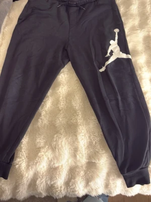 Svarta Jordan mjukisbyxor - Säljer ett par svarta mjukisbyxor från Jordan med den klassiska vita Jumpman-loggan på ena benet. Byxorna har resår i midjan med dragsko, sidofickor och muddar vid bensluten. Perfekta för chill eller träning.