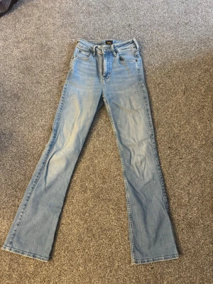 Ljusblå bootcut jeans från Lee - Säljer ett par ljusblå bootcut jeans från Lee med klassisk femficksmodell och dragkedjegylf. Jeansen har en rak passform upptill och lätt utsvängda ben. Tillverkade i mjuk denim med Lee-logga på bakfickan och läderpatch i midjan.