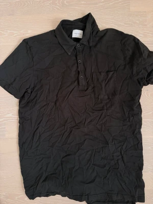 Svart kortärmad skjorta från Limitato - Stilren svart skjorta från ADays march med klassisk krage, korta ärmar och bröstficka. Skjortan har knappar framtill och är tillverkad i mjuk bomull som känns skön mot huden. Perfekt för en avslappnad men snygg look.