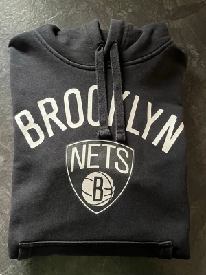 Brooklyn Nets hoodie - Snygg svart hoodie från New Era med Brooklyn Nets-logga och text i vitt på bröstet. Storlek XS , sitter hyfsat tajt. Passar bra från ålder 10-14. 