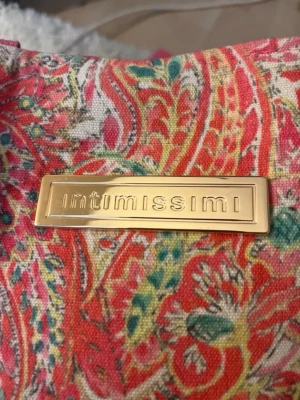 Skit snygg väska från Intimissimi💖 - Färgglad väska från Intimissimi med paisleymönster i rött, rosa, grönt och gult. Väskan har breda rosa axelband och en guldig logga framtill. Tillverkad i tyg, perfekt för att bära med sig allt man behöver.