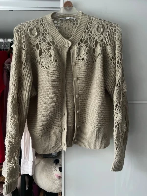 Grön stickad kofta med virkade detaljer - Säljer en grön stickad kofta med unika virkade spetsdetaljer på axlar och ärmar. Koftan har rund halsringning, knappar framtill. 