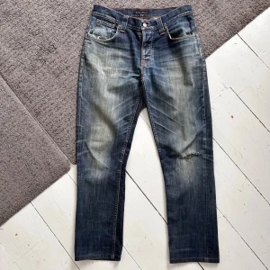 Mörkblåa Nudie Grim Tim Jeans - Riktigt feta Nudie jeans med sjuka fades. | W31 L32. | Riktigt bra skick, finns några små diskreta stilrena slitningar. | Väldigt tydliga honeycombs & whiskers. | Längd: 98cm, Midja: 38-43cm (Stretch). | Skriv vid minsta fundering, pris ej hugget i sten.