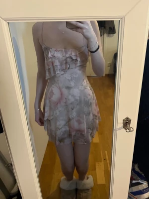 Blommig kortklänning med volang - Söt kortklänning med blommigt mönster i ljusa toner av beige, rosa och vitt. Klänningen har tunna axelband, volangdetaljer över bysten och en flowy kjol. Perfekt för sommarens alla tillfällen. Jag är 170cm som referens.